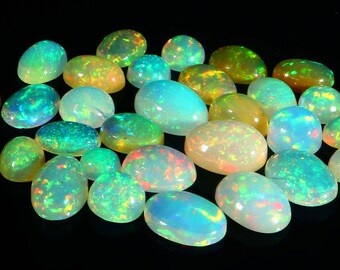 Puede incluir: Una colección de ópalos de forma ovalada en varios tonos de verde, azul y blanco. Los ópalos tienen una calidad brillante e iridiscente.