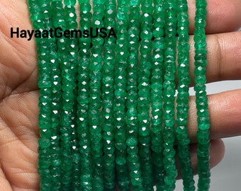 May include: A strand of emerald green faceted beads. The beads are small and round, and they are strung on a clear thread. The beads are arranged in a straight line, and they are all the same size and shape. The beads are a bright, vibrant green color.