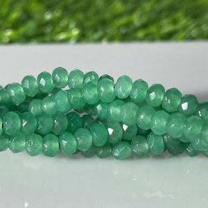 May include: A strand of green faceted gemstone beads. The beads are round and have a smooth, polished finish.