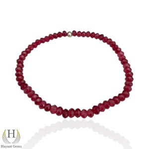 May include: A red gemstone bracelet with a silver clasp. The bracelet is made of small, faceted beads.