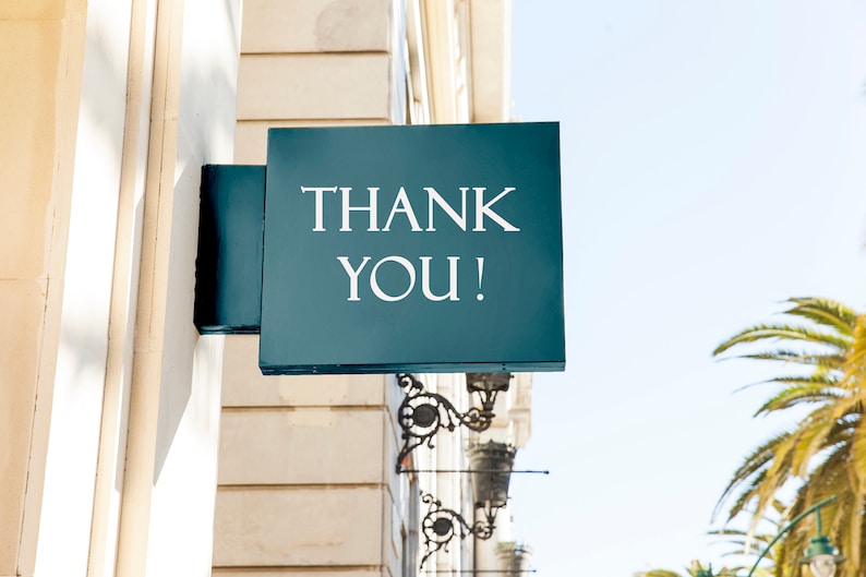 Może przedstawiać: Turkusowy znak z białym napisem "THANK YOU!", zamontowany na elewacji budynku. Znak jest kwadratowy i posiada ozdobny metalowy wspornik. W tle widoczne są palmy i czyste niebo.