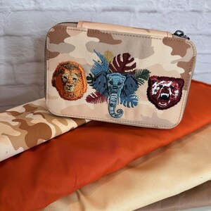 Könnte beinhalten: Eine Reißverschlusstasche mit Tarnmuster und gestickten Bildern von einem Löwen, einem Elefanten und einem Bären. Die Tasche ist aus einem weichen, strapazierfähigen Stoff gefertigt und hat einen Reißverschluss.