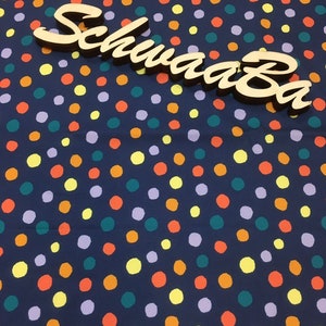 May include: A navy blue fabric with a polka dot pattern. The dots are in various colours, including yellow, orange, green, and purple. The word "SchwaaaBa" is written in a wooden font on top of the fabric.