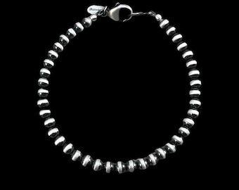May include: A silver bracelet with black and white beads. The bracelet is made of small, round beads that are arranged in a repeating pattern.