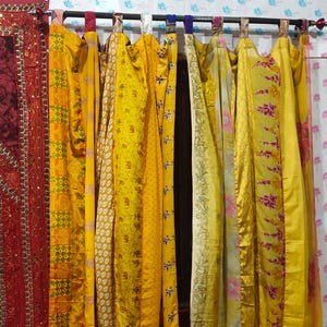 May include: A collection of yellow curtains with diverse patterns, including floral and geometric designs. The curtains are suspended from a dark rod, creating a warm atmosphere. The fabric appears lightweight and flowing, adding a touch of elegance to the room. The curtains are made of a lightweight fabric.