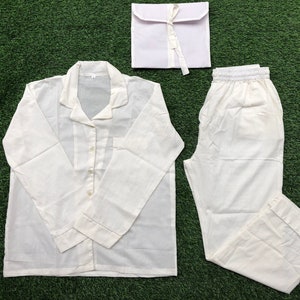 Può includere: Un pigiama bianco con una camicia a maniche lunghe e pantaloni. La camicia ha una chiusura con bottoni sul davanti e un colletto. I pantaloni hanno una cintura elastica.