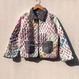 Puede incluir: Una chaqueta acolchada con un mosaico de patrones florales en varios colores, incluyendo rosa, azul y verde. La chaqueta tiene un cuello, puños y dos bolsillos delanteros a rayas blancas y negras, con el texto Naazcreation visible.