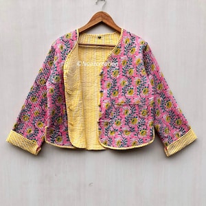 May include: A pink and yellow quilted jacket with a floral print. The jacket has a button closure and a pocket on the right side. The jacket is lined with a yellow and white striped fabric.