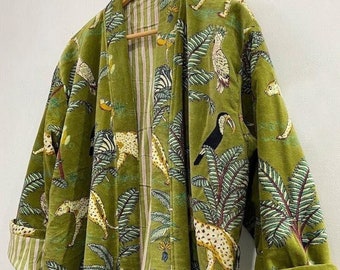 May include: A long-sleeved olive green robe featuring a repeating print of leopards, toucans, and palm trees. The garment has a folded collar and cuffs that reveal a white and red vertical striped lining, and it hangs on a wooden hanger.