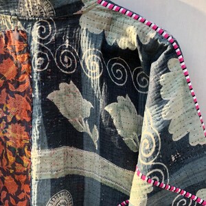 Puede incluir: Primer plano de una chaqueta patchwork con un estampado floral y de remolinos. La chaqueta presenta tejidos azul oscuro, naranja y verde claro. Los bordes est&aacute;n ribeteados con un borde a rayas rosa y blanco.