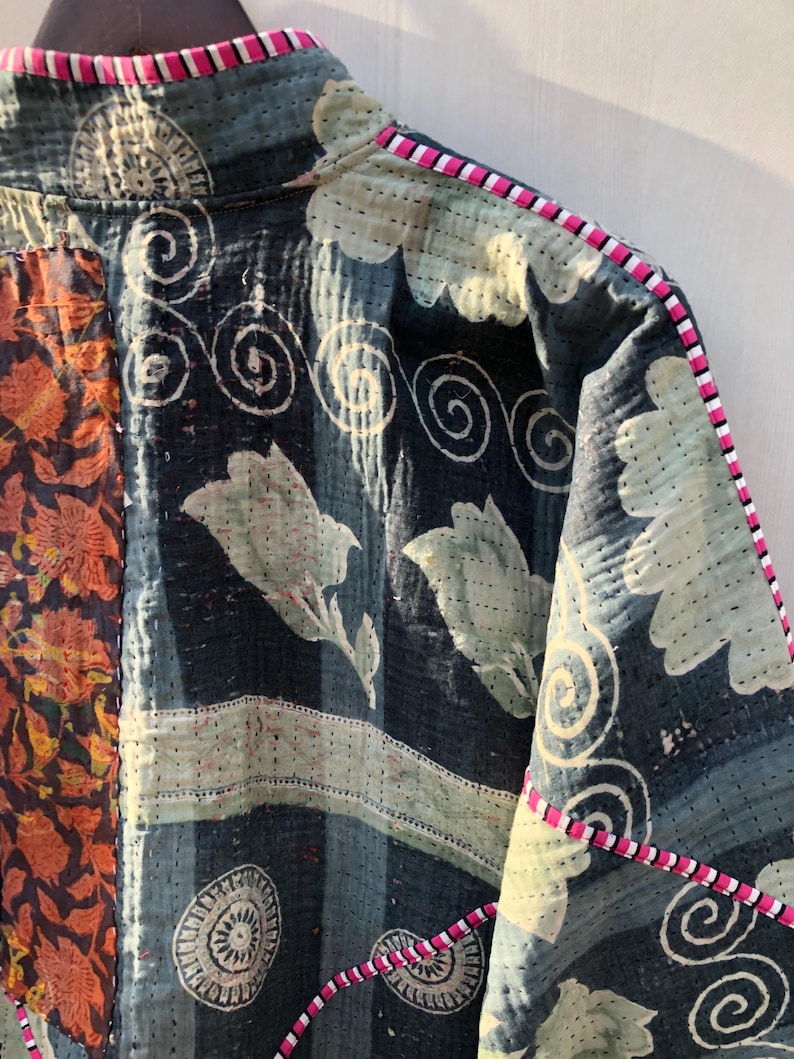 Puede incluir: Primer plano de una chaqueta patchwork con un estampado floral y de remolinos. La chaqueta presenta tejidos azul oscuro, naranja y verde claro. Los bordes est&aacute;n ribeteados con un borde a rayas rosa y blanco.