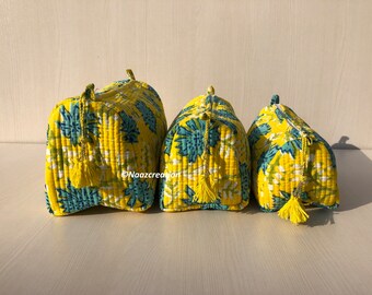 May include: Three yellow quilted makeup bags with blue floral patterns and tassels. The bags are lined up in order of size, with the largest bag on the left and the smallest bag on the right.