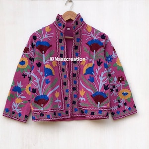 May include: A pink embroidered jacket featuring floral patterns in shades of blue, yellow, red, and green. The jacket has a mandarin collar and a front zip fastening. The text "©Naazcreation" is visible on the front of the jacket.