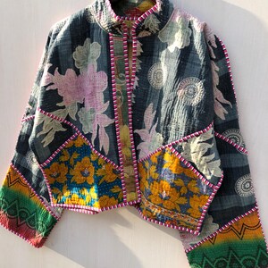 Puede incluir: Chaqueta patchwork con cuello alzado, con estampados florales y geom&eacute;tricos en tonos azul, amarillo, rosa y verde. La chaqueta tiene una textura acolchada y est&aacute; ribeteada con costuras rosas.