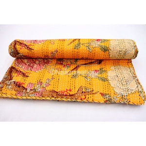 May include: A yellow kantha quilt with a floral print. The quilt is folded and rolled up, showing the intricate hand-stitching details.