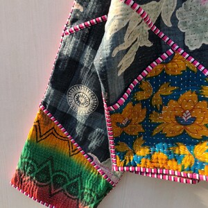 Puede incluir: Chaqueta patchwork con una variedad de patrones y colores. La chaqueta presenta una tela azul oscuro con un dise&ntilde;o circular blanco, un estampado floral en amarillo y azul, y una secci&oacute;n de colores del arco&iacute;ris. Ribetes rosas y blancos delinean las costuras.