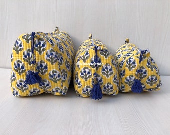 May include: Three yellow quilted makeup bags with blue floral patterns and blue tassels. The bags are lined up in order of size, with the largest bag on the left and the smallest bag on the right.