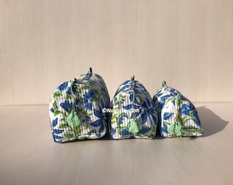 May include: Three quilted fabric cosmetic bags in different sizes. The bags are white with a blue and green floral pattern. Each bag has a light green tassel.