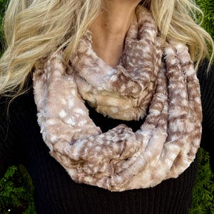 May include: A faux fur infinity scarf in shades of brown and cream. The soft, plush scarf is wrapped around the neck, creating a warm and stylish accessory. The scarf has a spotted pattern and is made of a soft, textured material.