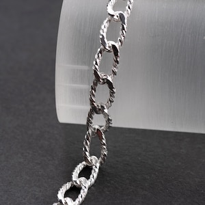 Könnte beinhalten: Ein silbernes Kettenarmband mit einem gedrehten Gliederdesign.