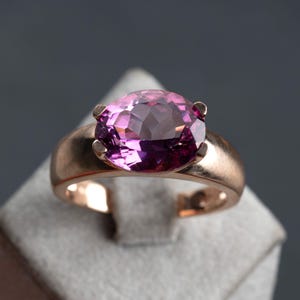 May include: A rose gold ring with a large, oval-shaped, purple gemstone.