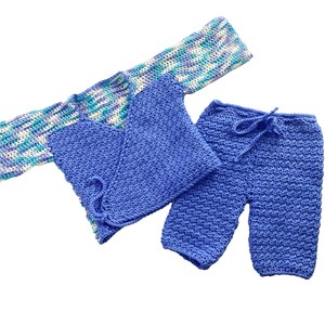 Puede incluir: Un conjunto de bebé de crochet azul con una parte superior de manga larga y pantalones. La parte superior tiene un diseño estampado blanco y azul en las mangas.