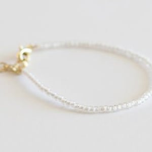 May include: A delicate white beaded bracelet with a gold clasp.
