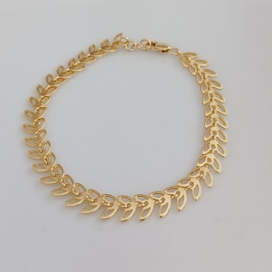 May include: A gold-toned bracelet with a delicate leaf design. The bracelet is made of metal and has a clasp closure.