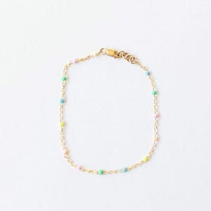 May include: A delicate gold-toned bracelet featuring a chain with small, colorful beads. The beads are pastel shades of pink, yellow, blue, and green. The bracelet has a clasp closure and is displayed on a white background.