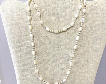 May include: A long necklace featuring a repeating pattern of smooth, oval-shaped off-white beads interspersed with small, metallic silver-toned spacer beads. The strand is arranged in a double-loop configuration, showcasing a consistent design.