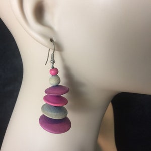 May include: Pink, gray, and blue wooden dangle earrings with a silver hook. The earrings are made of stacked wooden discs and beads.