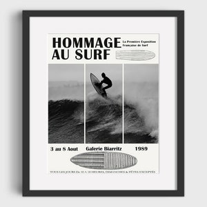 Op de afbeelding: Een zwart-wit poster die een surfen tentoonstelling in Biarritz, Frankrijk, adverteert. De poster toont een surfer op een golf, een surfboard en de tekst "Hommage au Surf", "La Premiere Exposition Française de Surf", "3 au 8 Aout", "Galerie Biarritz", "1989" en "Tous les jours de 10 à 18 heures, dimanches & fêtes exceptés".