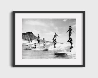 May include: A black and white photograph of a group of people surfing on a beach. The people are standing on surfboards and are riding the waves. There is a mountain in the background.