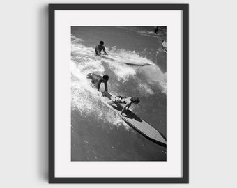 May include: Black and white photograph of three people surfing on longboards in a wave. The surfers are all wearing swimsuits and are riding the waves with their arms outstretched.