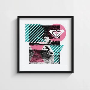 Op de afbeelding: Een ingelijste vierkante muurkunstprint met een zwart-witfoto van een surfer op een golf. Het ontwerp bevat het woord ROXY in grote letters, met diagonale blauwgroene strepen, een roze cirkel en een wit hartvormig logo als overlay.