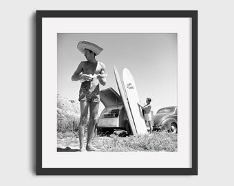 May include: Black and white photo of two people standing next to a vintage car and surfboards. One person is wearing a wide-brimmed hat and playing a ukulele. The surfboard has the text "Lani Kai" written on it.