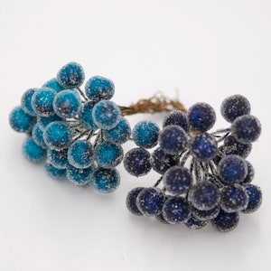 May include: Two bunches of faux berries, one blue and one dark blue, with a frosted finish. The berries are clustered together on thin wire stems.