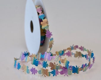 May include: A spool of colorful ribbon with a repeating pattern of butterflies and flowers. The ribbon is a light blue, pink, yellow, and green.