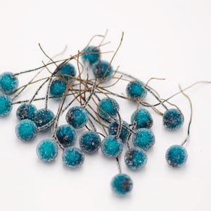 May include: A cluster of teal blue berry-shaped ornaments with a frosted finish, attached to thin brown wire stems.