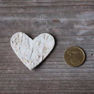 May include: A white wooden heart-shaped ornament and a gold coin with the text "5 groszy" on a wooden surface.