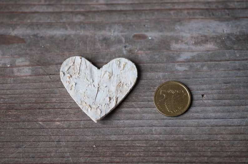 May include: A white wooden heart-shaped ornament and a gold coin with the text "5 groszy" on a wooden surface.