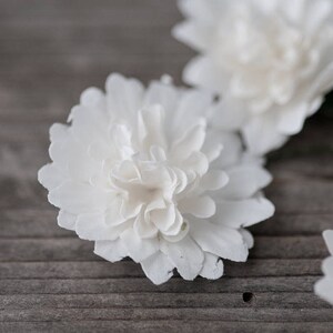 May include: Three white paper flowers on a wooden surface. The flowers are made of paper and have a delicate, ruffled texture.