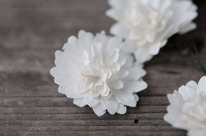 May include: Three white paper flowers on a wooden surface. The flowers are made of paper and have a delicate, ruffled texture.