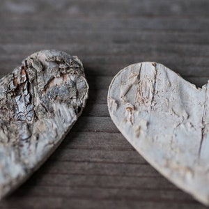 May include: Two heart-shaped pieces of wood, carved from birch bark, with a natural, rustic finish. The wood has a light gray color and a textured surface.