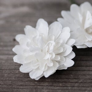 May include: Three white paper flowers with delicate, layered petals. The flowers are arranged on a wooden surface.