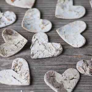May include: A collection of white wooden hearts with a rustic, textured finish. The hearts are arranged on a wooden surface.