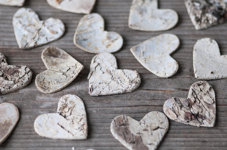 May include: A collection of white wooden hearts with a rustic, textured finish. The hearts are arranged on a wooden surface.