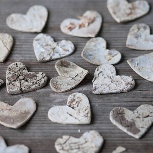 May include: A collection of white wooden hearts with a rustic, textured finish. The hearts are scattered on a wooden surface.