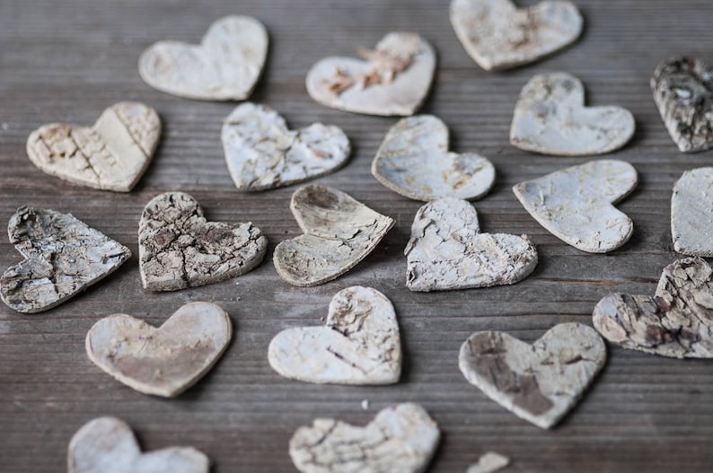 May include: A collection of white wooden hearts with a rustic, textured finish. The hearts are scattered on a wooden surface.