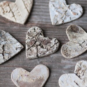 May include: A collection of rustic, white, wooden heart-shaped ornaments with a natural, bark-like texture. The hearts are arranged on a wooden surface.